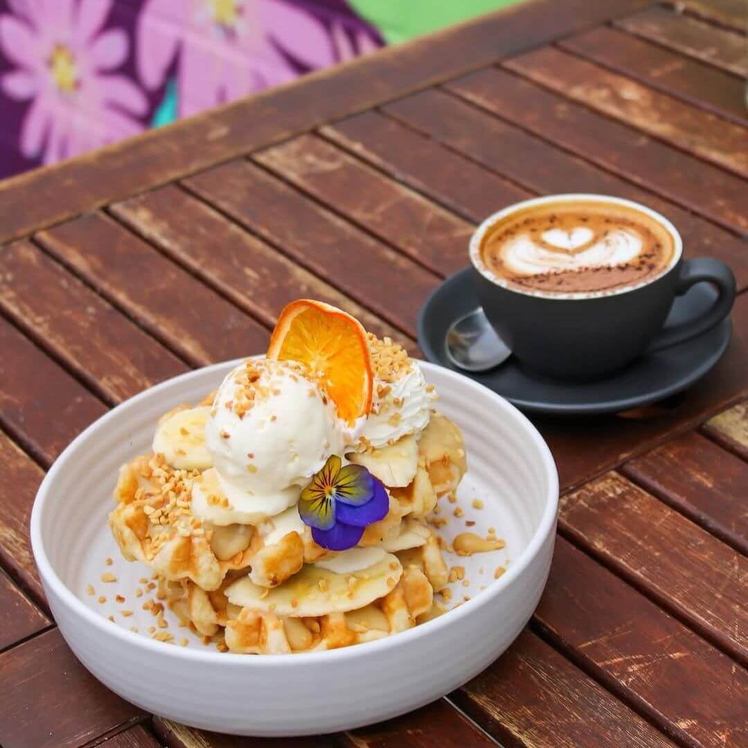 A bowl of freshly cooked waffles with a cup of coffee behind it.